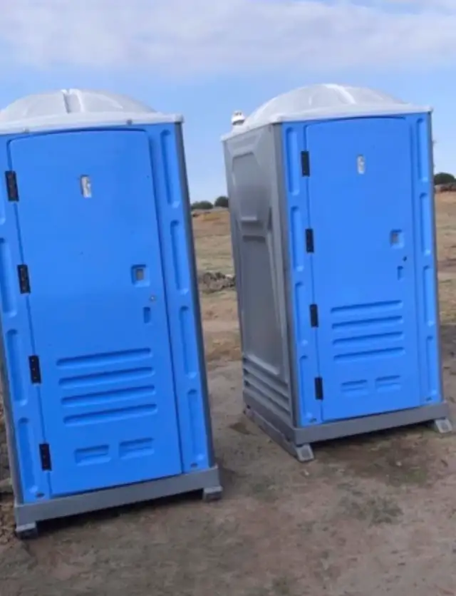 Blue and gray porta potties set on a dirt construction lot