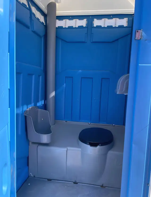 Clean interior of a blue standard porta potty with seat, urinal and vent pipe