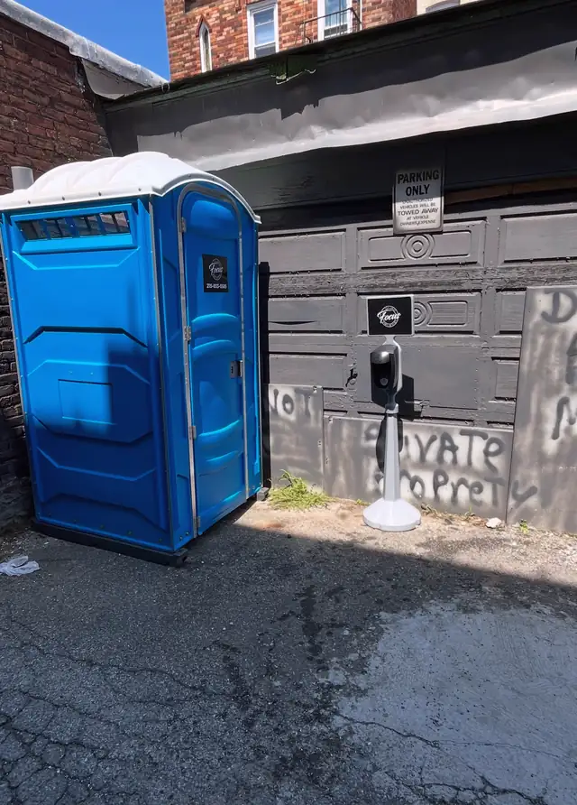 Blue porta potty placed off the pavement beside a garage
