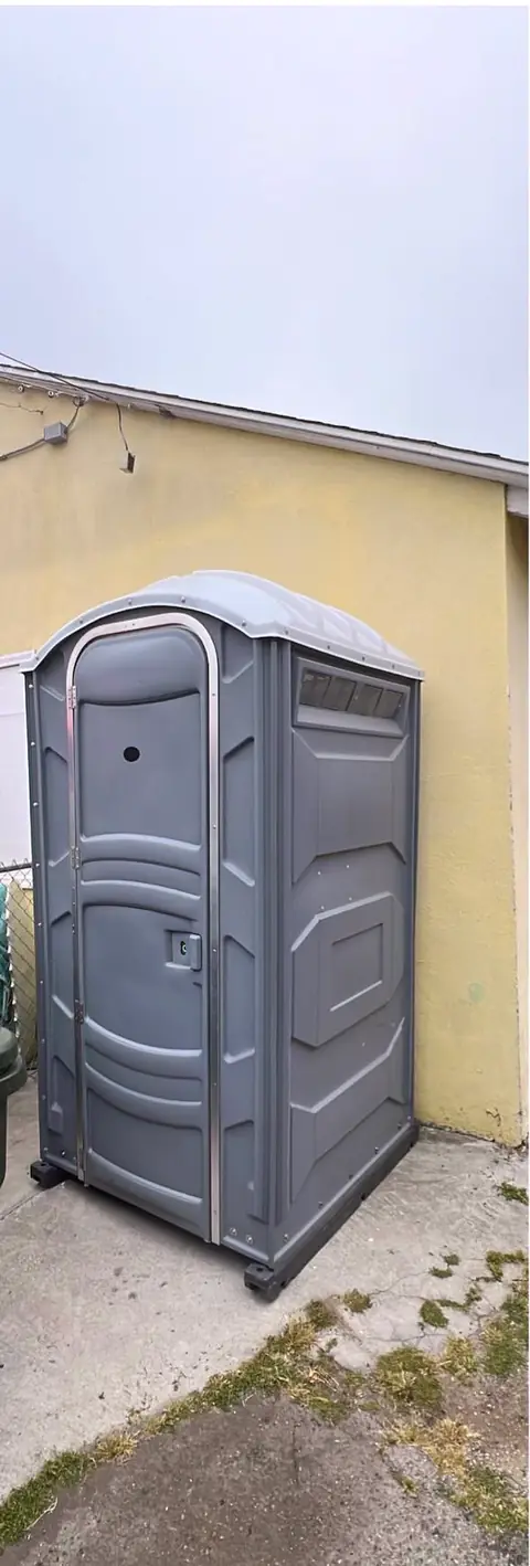 Gray porta potty in a narrow side yard next to a house