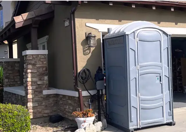 Gray porta potty set on a driveway beside a house remodel